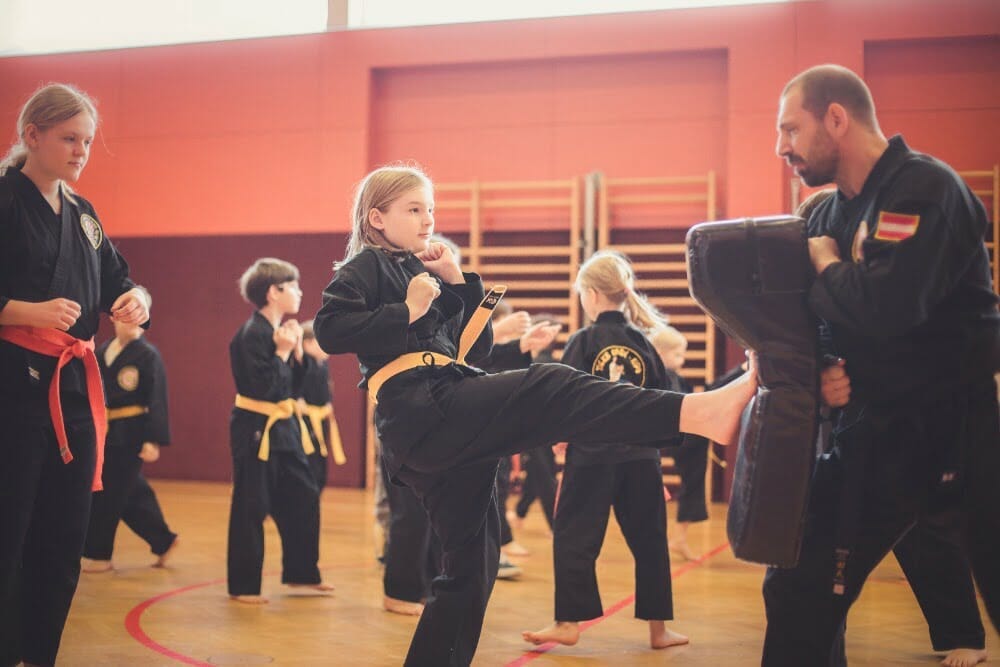 Entschlossene Karateschülerin perfektioniert Vorwärtstritt anhand eines großen Schlagpolsters, unterstützt von ihrem aufmerksamen Lehrer.
